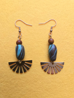 Blue Swirl Clay & Brass Sunrays Earrings Dangle Earrings with blue & brown swirl clay beads, topped with small lighter brown wood beads, and accented with a brass charm that resembles sunrays. Earrings are 2.5 inches long with 18k gold plated earring hooks