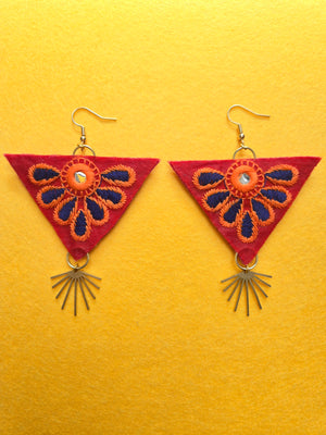 Blue Petal Triangle Earrings Red inverted triangle with a blue and orange embroidered petal overlay, surrounding a small circle shaped mirror, in the center of the inverted triangle. Connected at the bottom point of the inverted triangle is brushed brass charm that resembles golden sunrays. The ear wires are plated in 18k gold and lined with polyester felt for comfort. Earrings are 4 inches long and 2.5 inches wide.