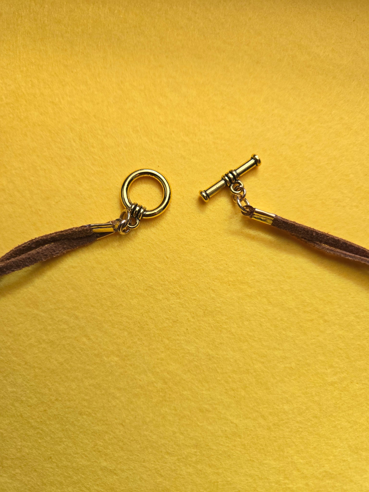 Closure is a toggle clasp on loosely twisted tan sueded leather.