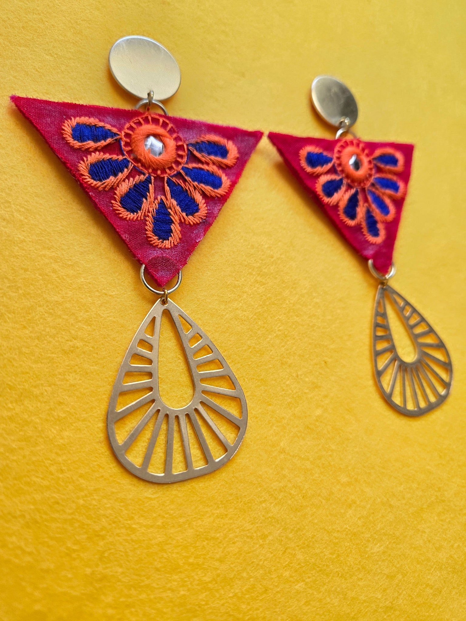 Brass Stud Embroidered Invented Triangle Earrings Stud Red Inverted triangle with a blue and orange embroidered petal overlay, surrounding a small circle shaped mirror, in the center of the inverted triangle. The stud portion of the earrings is a brushed brass circle shape. Connected to the point of the inverted triangle is a brushed brass cut-out teardrop shape. The post is plated in 18k gold and lined with polyester felt for comfort. Earrings are 4.5 inches long and 2.5 inches wide