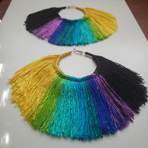 This image shows a close up of how the colors of the earrings look. Fan shaped Multi-Colored Tassel Hoop earrings that are yellow, lime-green, blue, purple, and black. Made with satin thread