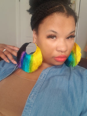This image shows how these earrings look on. Fan shaped Multi-Colored Tassel Hoop earrings that are yellow, lime-green, blue, purple, and black. Made with satin thread